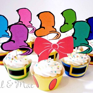 Puede incluir: Un conjunto de adornos para cupcakes coloridos con sombreros caprichosos y un lazo rojo. Los adornos son perfectos para una fiesta de cumpleaños o una ocasión especial.