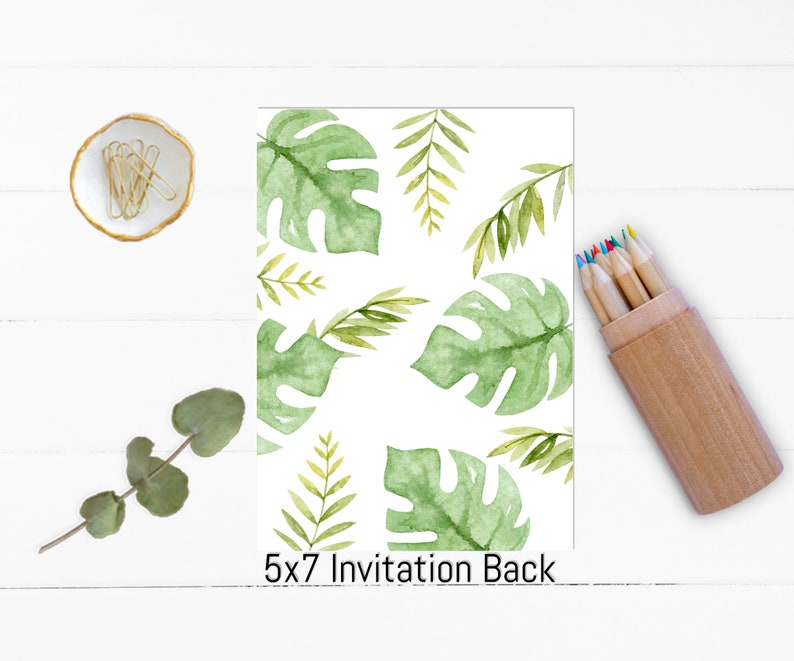 May include: A 5x7 invitation back with a watercolor design of green tropical leaves on a white background. A small dish with gold paper clips, a sprig of eucalyptus, and a wooden pencil holder with colored pencils are also visible.