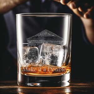 May include: A clear glass with a design of a building etched on the side. The glass is filled with amber liquid and ice cubes. The text "Make it a Double" is printed on the glass.