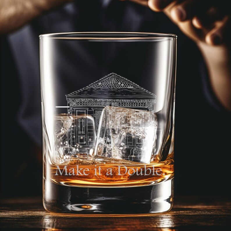 May include: A clear glass with a design of a building etched on the side. The glass is filled with amber liquid and ice cubes. The text "Make it a Double" is printed on the glass.