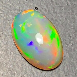 May include: A polished, oval-shaped opal gemstone. The opal displays a milky white base color with vibrant flashes of green, orange, and blue, creating a play-of-color effect. The gemstone is smooth and reflective, showcasing its natural beauty.