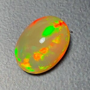 May include: Oval-shaped opal gemstone with a translucent body. The opal displays vibrant flashes of green, orange, and red colors throughout its surface. The gemstone is set against a gray background.