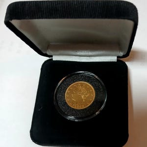 May include: A gold coin displayed in a black velvet presentation box. The coin is encased in a clear plastic holder. The coin has intricate details and appears to be from 1908. The box is open, revealing the coin against a black interior.
