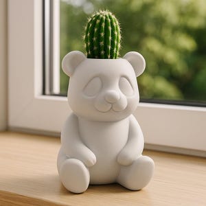 Puede incluir: Una maceta blanca con forma de panda que contiene un cactus verde. La maceta tiene una cara sonriente y está colocada sobre una superficie de madera. El fondo es un follaje verde borroso.
