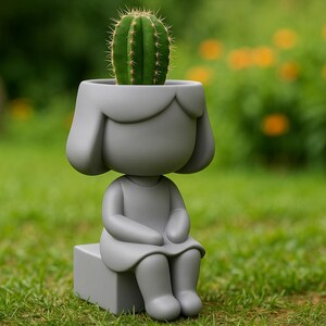 May include: A gray ceramic planter shaped like a seated figure with a cactus planted in its head. The figure is sitting on a small block, with a green lawn and blurred background of foliage. The planter is a unique decorative item.
