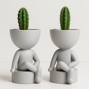 Könnte beinhalten: Zwei graue Keramik-Pflanzgefäße in Form von Figuren, die jeweils einen grünen Kaktus halten. Die Pflanzgefäße haben ein minimalistisches Design mit rundem Kopf und sitzender Pose. Die Kakteen sind leuchtend grün.