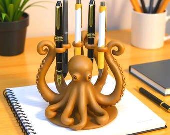 May include: A brown octopus pen holder with several pens. The pen holder is on a desk with a notebook and a plant in the background. The pens are black, white, and gold.
