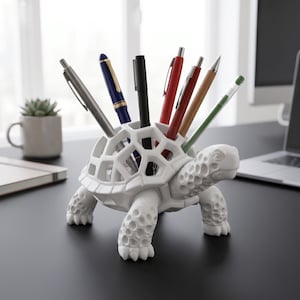 May include: A white turtle-shaped pen holder with a honeycomb shell design. The holder contains pens in silver, blue, red, and green. The pen holder is on a black desk. The desk is likely in an office.