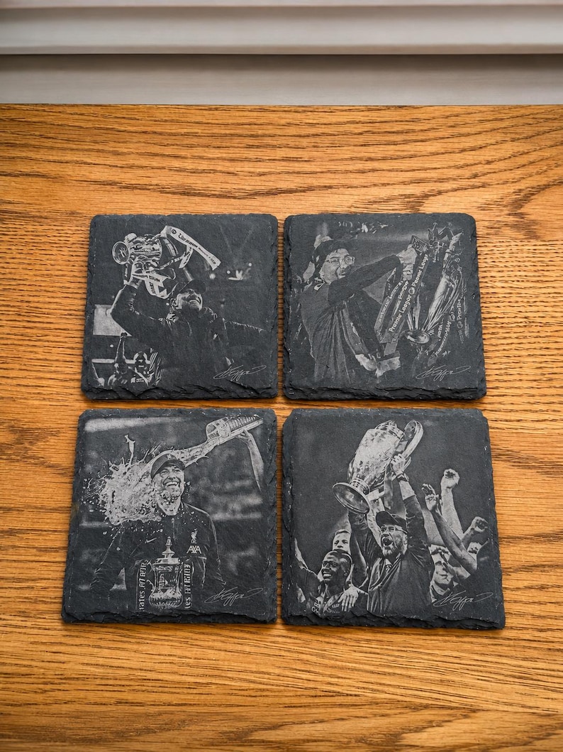 May include: Four square black slate coasters featuring laser-engraved images of a soccer manager celebrating with various trophies. Each coaster displays a distinct scene of victory, including a person holding a cup and a signature at the bottom.