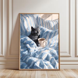 May include: A framed art print depicts a gray cat lounging on a blue and white striped blanket with a coffee mug. The artwork has a cozy, relaxed theme, with soft lighting and a warm color palette. The cat is the focal point, with a serene expression.