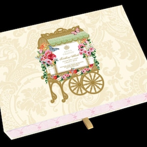 May include: A rectangular cream-colored craft box featuring a damask pattern and a central illustration of a flower cart. The cart is adorned with pink and red flowers, green foliage, and butterflies. Text reads Anna Griffin Finishing School.