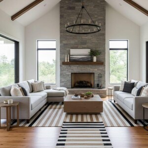 May include: A contemporary living room with a stone fireplace, two light grey sofas, and a wooden coffee table. A striped rug and hardwood floors add warmth. The room features large windows and a chandelier.