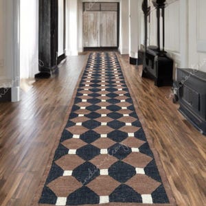 Puede incluir: Una alfombra larga y rectangular con un patrón geométrico de diamantes marrones, azul marino y blancos. La alfombra tiene un borde con flecos y está colocada sobre un suelo de madera en un pasillo. El pasillo tiene paredes blancas y detalles oscuros.