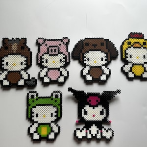 Puede incluir: Una colección de seis figuras de pixel art, cada una representando un personaje de gato blanco con varios disfraces. Las figuras están hechas de cuentas de colores, incluyendo marrón, rosa, negro, verde y amarillo. Las figuras están dispuestas sobre una superficie blanca.