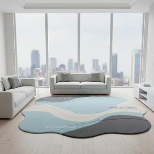 May include: A modern living room featuring a light blue, gray, and white abstract rug. The rug is in front of a white sofa and a large window with a city view. The text "WHITE ISLAND RUGS" is visible on the rug.