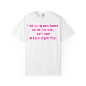 May include: White t-shirt featuring the pink text: "I just had my salad tossed, ass ate, ass eaten, I don't know, I'm not an English major." The shirt has a crew neck and short sleeves.