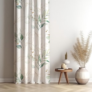 Könnte beinhalten: Weißer Vorhang mit einem botanischen Design mit grünen Blättern und goldfarbenen Umrissen. Der Vorhang hängt vor einer weißen Wand. Das Design umfasst kleine goldfarbene Akzente.