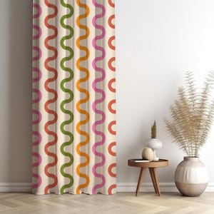 May include: A cream-coloured curtain featuring a repeating wavy pattern in red, green, orange, and pink. The curtain hangs in front of a white wall, with a small wooden table and decorative vases nearby.