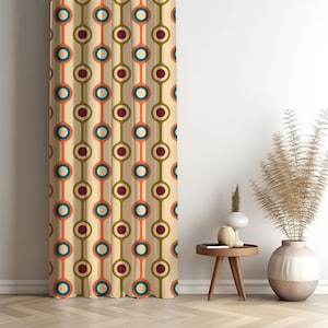 May include: A beige curtain with a retro pattern of connected circles in teal, orange, and burgundy. The curtain hangs in front of a white wall, with a small wooden table and decorative vase nearby. The design is reminiscent of the 1970s.