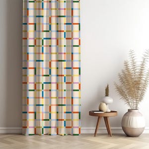 May include: A beige curtain with a colorful grid pattern of rectangles in shades of red, blue, green, yellow, and purple. The curtain is hanging in front of a white wall, with a small wooden table and decorative vases nearby.