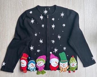 May include: A black long-sleeve zip-up cardigan featuring white embroidered snowflakes across the upper portion and six colourful snowman appliqués along the bottom hem, each wearing a unique hat and scarf in red, blue, pink, green, and yellow.