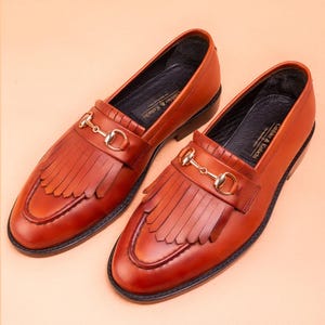 Handmade brown leather fringe loafers for men with metal bit detail, premium slip-on formal dress shoes crafted from genuine leather for weddings and business wear.