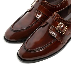 May include: A pair of polished brown leather dress shoes. The shoes feature a glossy finish, decorative stitching, and a buckle closure. The design includes a rounded toe and a low heel, suitable for formal occasions.