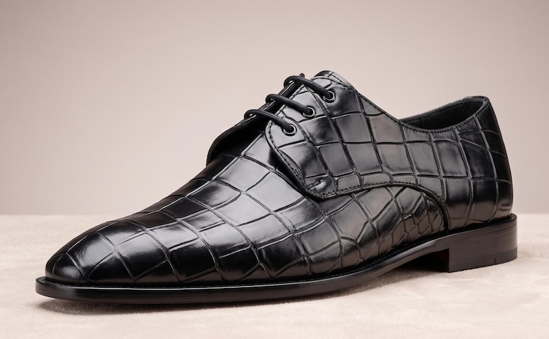 May include: A black dress shoe with a glossy finish and a textured crocodile skin pattern. The shoe features a rounded toe, a low heel, and black laces threaded through four eyelets on each side of the central tongue area.