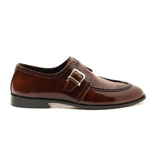 May include: A brown leather dress shoe with a buckle closure. The shoe has a glossy finish and a black sole. The buckle is gold-colored. The shoe has decorative stitching along the edges.