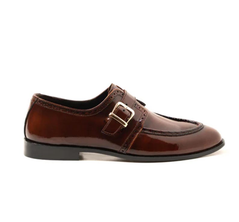 May include: A brown leather dress shoe with a buckle closure. The shoe has a glossy finish and a black sole. The buckle is gold-colored. The shoe has decorative stitching along the edges.