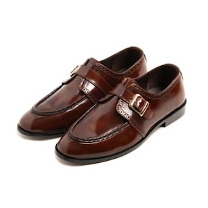 May include: A pair of polished brown leather shoes with a buckle closure. The shoes have a classic design with decorative stitching and a glossy finish. The shoes are a size 10.