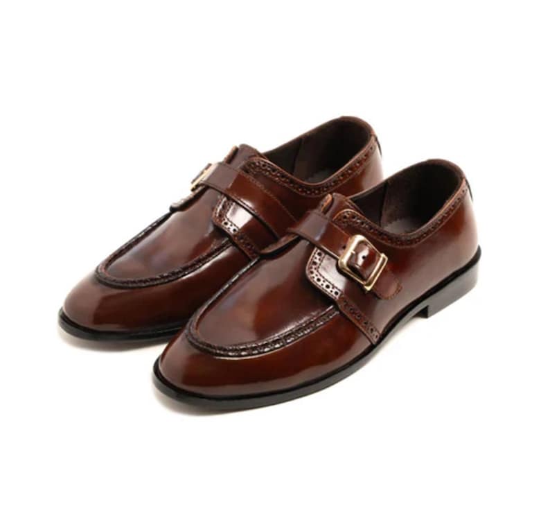 May include: A pair of polished brown leather shoes with a buckle closure. The shoes have a classic design with decorative stitching and a glossy finish. The shoes are a size 10.