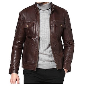 May include: A brown leather jacket with a stand-up collar and two chest pockets. The jacket has a full-length zipper and two lower pockets. The model is wearing a gray sweater underneath the jacket.