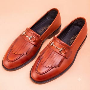 Handmade brown leather fringe loafers for men with metal bit detail, premium slip-on formal dress shoes crafted from genuine leather for weddings and business wear.