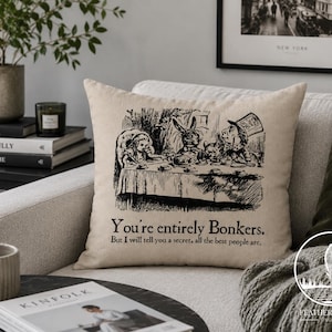 May include: Beige throw pillow with a black and white illustration of the Mad Hatter's tea party from Alice in Wonderland. The text "You're entirely Bonkers" is printed below the illustration.