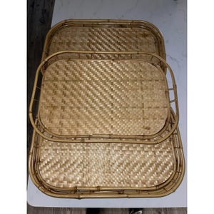 May include: Set of three woven bamboo trays in varying sizes. The trays have a rectangular shape with rounded corners and woven basket weave pattern. The edges are framed with bamboo. The trays are a light brown color.