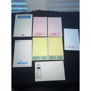 May include: A collection of seven rectangular pharmaceutical promotional notepads. The pads feature various brand names including Bronkometer-2, Septra DS, Gyne-Lotrimin, Actifed Syrup, and Travil 4-50, displayed in white, pink, yellow, and blue color schemes.