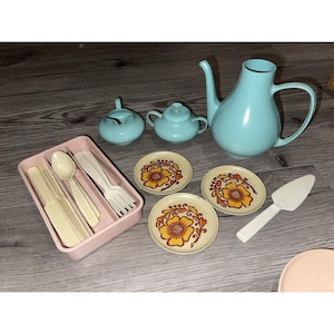 May include: A vintage toy tea set with a light blue teapot, sugar bowl, and creamer. Includes small plates with orange floral designs, a pink cutlery tray with utensils, and a white cake server.