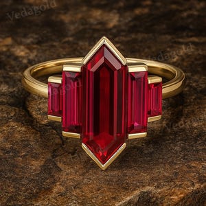 以下が含まれることがあります： 中央に大きな長方形の濃い赤色の宝石をあしらい、両側に2つの小さな長方形の赤い宝石を配したゴールドリング。リングはシンプルでエレガントなデザインです。