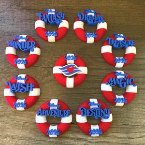 May include: A collection of red, white, and blue decorative life preservers with various Disney cruise ship names in blue script. Each ring has the year 2026 printed on it. The central ring features the Disney Cruise Line logo.