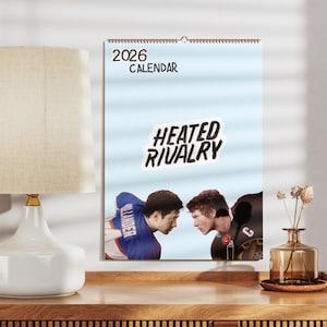 Könnte beinhalten: Ein Kalender für 2026 mit hellblauem Hintergrund zeigt zwei Athleten, die sich gegenüberstehen. Der Text "HEATED RIVALRY" befindet sich über den Athleten. Das Wort "CALENDAR" steht oben.