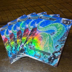Può includere: Un set di quattro carte collezionabili identiche raffiguranti un grande tentacolo verde traslucido che emerge dall'acqua blu. Le carte riportano il testo Tentacle, Token Unit - Bilgewater e The depths do not bargain. They reach out and take.