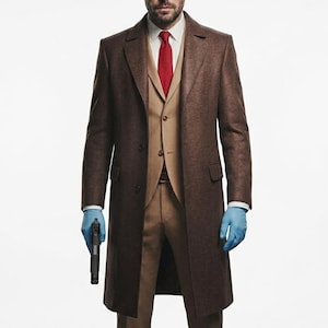 Może przedstawiać: Brązowy płaszcz z pasującym garniturem i czerwoną krawatem. Garnitur jest beżowy, a płaszcz ciemniejszy brązowy. Osoba ma na sobie niebieskie rękawiczki i trzyma czarny pistolet.