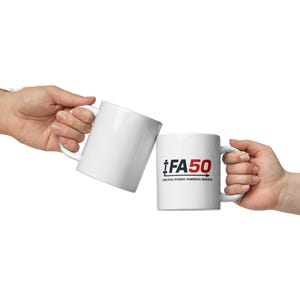 May include: Two white ceramic mugs are held in hands against a white backdrop. One mug features the text "FA50" in black and red, with the words "PRACTICAL FITNESS. POWERFUL RESULTS." below. The other mug is plain white.