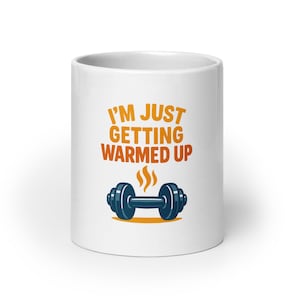 May include: White ceramic mug featuring the text "I'M JUST GETTING WARMED UP" in orange and red. A blue dumbbell with orange steam is below the text. The mug is designed for fitness enthusiasts.
