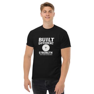 May include: Black t-shirt featuring the white text "BUILT DIFFERENT" above a cross symbol and the words "STRENGTH THAT STARTS IN THE SOUL". The shirt has a crew neck design.