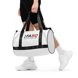 May include: White cylindrical duffel bag with black handles and trim. The bag displays the text "iFA50" in black and red, with the tagline "PRACTICAL FITNESS. POWERFUL RESULTS." The bag is held by a person wearing black shorts and white trainers.