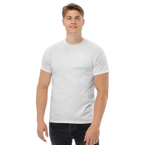 May include: Light gray t-shirt with short sleeves. The shirt has the text "Propagation of Misinformation" printed in a light teal color on the upper left chest. The shirt is made of a soft material.