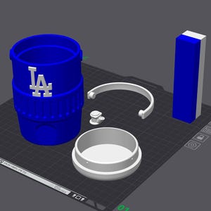 Könnte beinhalten: Ein blau-weißer 3D-gedruckter Becher mit dem Logo der LA Dodgers. Der Becher ist zerlegt und zeigt den Hauptbecher, einen Deckel, einen Griff und ein rechteckiges Stück. Die Teile sind auf einer dunkelgrauen Oberfläche angeordnet.