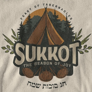 Może przedstawiać: Kremowa koszulka z grafiką w stylu vintage. Projekt zawiera brązowy namiot, drzewa i słowo "SUKKOT" dużymi literami. Tekst brzmi "FEAST OF TABERNACLES" i "THE SEASON OF JOY".